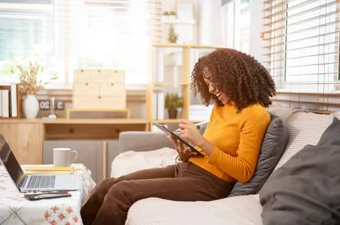 A side view image of a happy Black woman is using her digital tablet on a c.. Stock Photos
