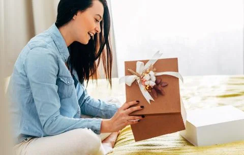Side view image of happy young woman sit on the bed unpacking the parcel rece Stock Photos