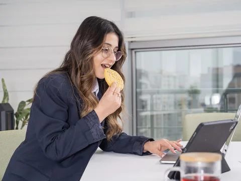 Side view image of young caucasian businesswoman eating cookie Stock Photos