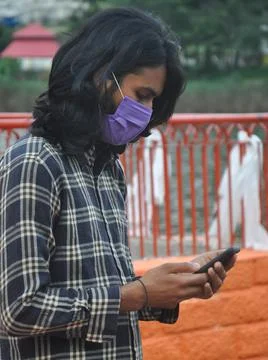 Side view of a Indian long haired young man wearing face mask with using phone Stock-Fotos