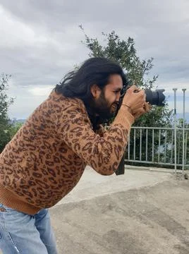Side view of a Indian long haired and bearded young man taking photo with camera Stock Photos