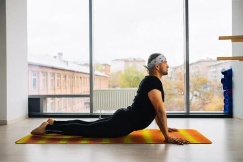 Side view of indian man doing the cobra pose in a bright fitness studio Foto stock