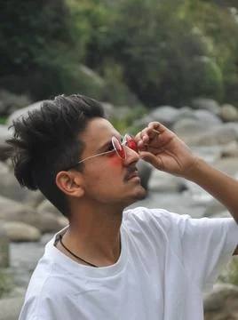 Side view of a Indian young guy adjusting his sunglasses while standing outdoor  Stock Photos