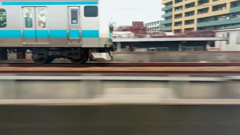 Side view of a Japanese commuter train with light blue stripes moving on tracks. Stock Footage 334578676