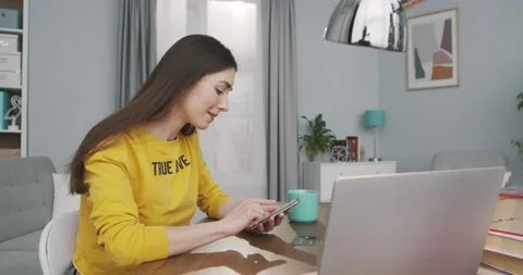Side view of joyful pretty young girl tapping on smartphone while sitting at Stock Footage 134718562