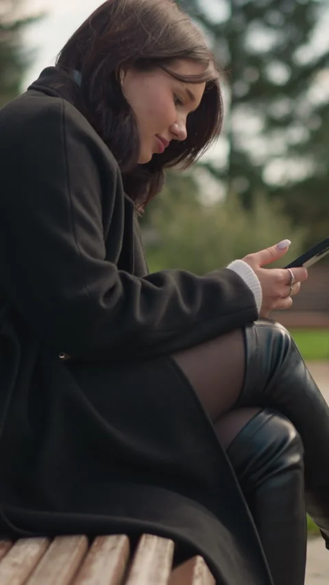 Side View Lady in Black Coat Using Phone While Sitting on Park Bench Video stock 310342567