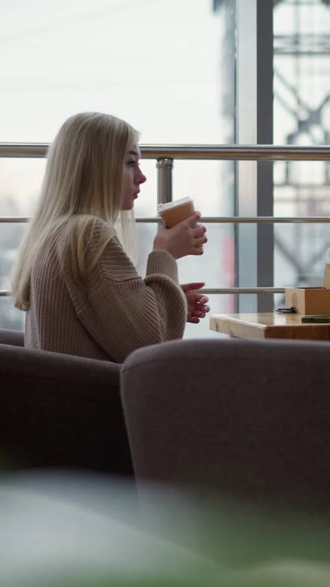 Side view of lady sipping coffee in mall with blurred urban view outside Stock-Footage 318214674