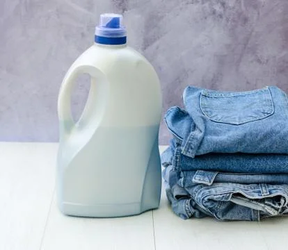 Side view of a large plastic bottle of liquid powder and a stack of denim ite Stock Photos