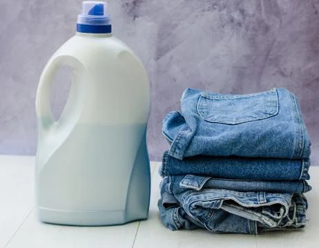 Side view of a large plastic bottle of liquid powder and a stack of denim ite Stock Photos