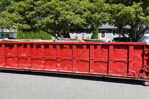 Side view of a large red beat up dumpster on the street by a curb in a reside Stock Photos