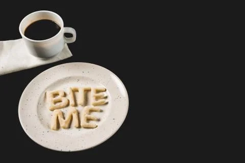 Side view of lettering bite me made from cookie dough on plate with coffee cu Foto stock
