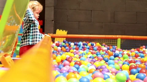 Side view of little blonde boy playing on trampoline with many colored balls 스톡 동영상 113343502