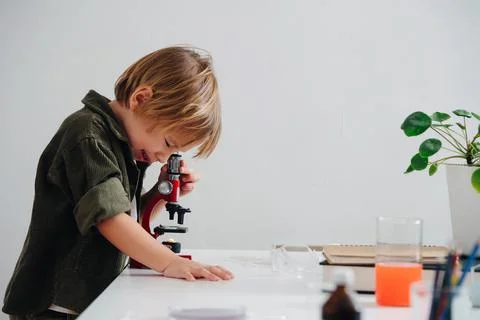 Side view little boy doing science project, looking through the microscope Stock Photos
