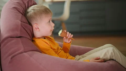 Side View Of Little Boy In Orange Shirt Relaxing And Eating Ice Cream Cone Stock-Footage 306625735