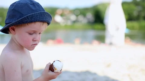 Side view of little cute happy blonde boy eating tasty ice-cream on sunny beach  스톡 동영상 137452529