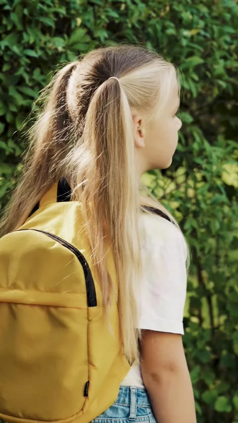 Side view of little schoolgirl with backpack walking outdoors vertical video Stockbeeldmateriaal 341522838