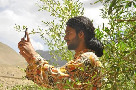 Side view of a long haired and bearded young guy taking photo with his phone Stock Photos