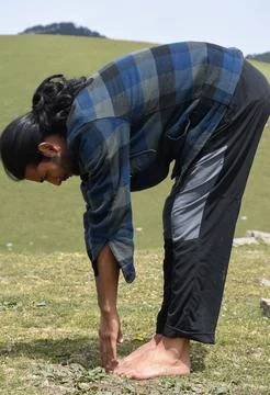 Side view of a long haired Indian young guy doing Uttanasana Yoga Pose  Stock Photos