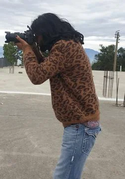 Side view of a long haired young man photographer taking photo with DSLR camera  Stock Photos