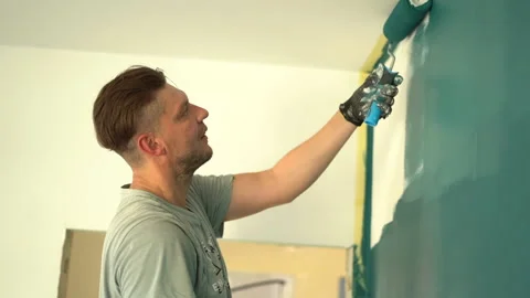 Side view, low angle shot. A young man paints a wall with a paint roller from Stock Footage 169664883