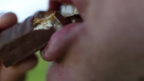 Side view macro of a person taking a bite of a chocolate bar with visible creamy Video stock 306000132