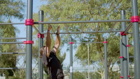 Side view of male athlete working out on monkey bars outside. Video stock 227135158