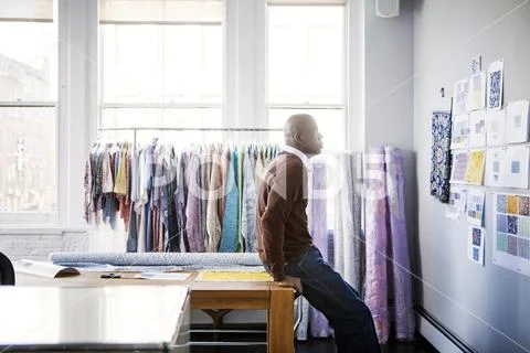 Side view of male fashion designer looking at designs on wall in workshop Stock Photos