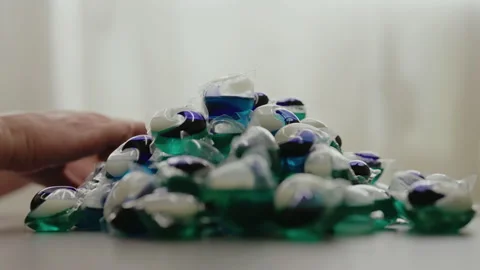 Side view of male hand taking colorful laundry detergent pod sitting at table Stock Footage 312352633