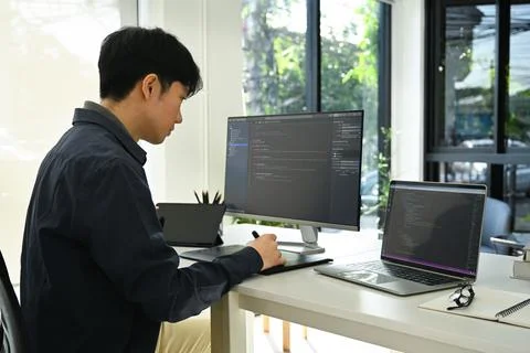 Side view of male programmer sitting front of computers with coded data on Stockfoto's