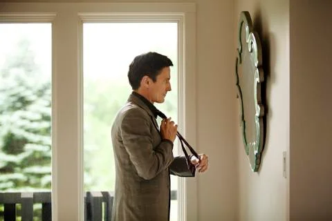 Side view of man adjusting tie while looking at mirror Stock Photos