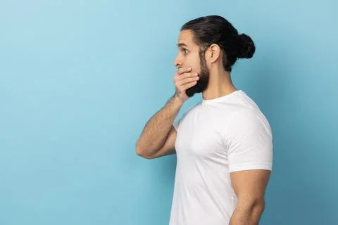 Side view of man with beard wearing white T-shirt covering mouth, doesnt want to Stock Photos