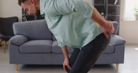 Side view of man bending with lower back pain while standing near sofa at home Stock Footage 317778906