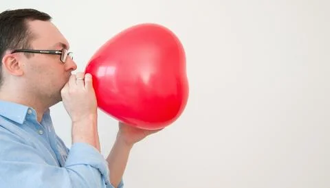 Side view on a man blowing heart balloon preparing for valentines day or an.. Stock Photos
