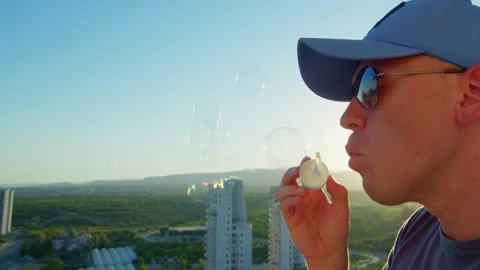 A side view of a man in a blue cap and sunglasses blowing soap bubbles Stock-Footage 331195861