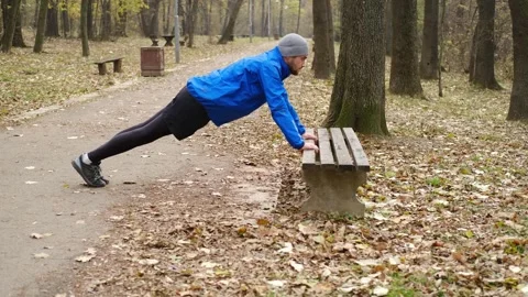 Side view of man in blue sports jacket doing push-ups on bench in autumn park Stock Footage 316820904