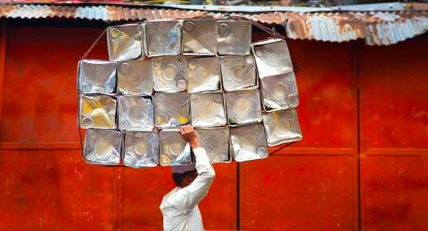 Side view of man carrying stack of metal containers on his head, walking past Foto stock