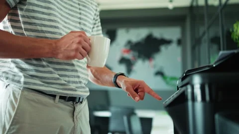 Side view of man with cup of coffee prints documents on printer in office 動画素材 244258247