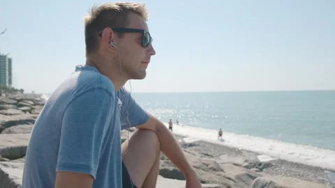 Side view of man with earphones on beach listening music using mobile phone Stock Footage 252148141