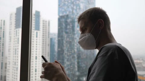 Side view of a man in a face mask using his smartphone sitting alone by the Stock Footage 155948160