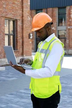 Side view of the man foreman in reflective vest and white helmet using portable Stock Photos