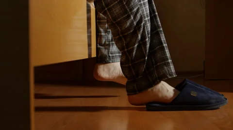 SIDE VIEW: Man gets up from a bed in the night then wears a slippers and goes Vídeo Stock 65173134