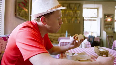 Side view of a man in a hat eating fast food in a cafe, camera movement Stock Footage 135613855