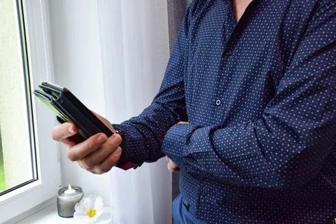 Side view of man holding smartphone in black case standing near window at home Stock Photos