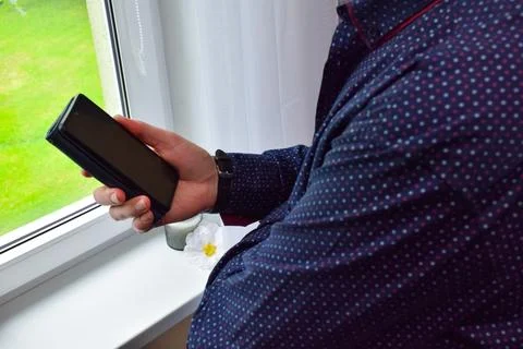 Side view of man holding smartphone in black case standing near window at home Stock Photos