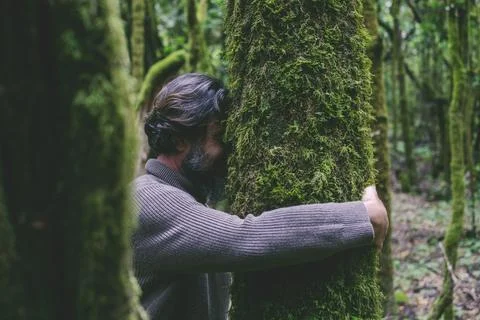Side view of a man hugging a tree with green musk. Concept of people nature l Stock Photos