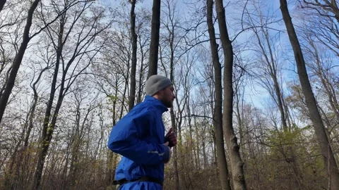 Side view of a man jogging in the autumn forest, wearing a blue jacket and grey Stock Footage 316837151
