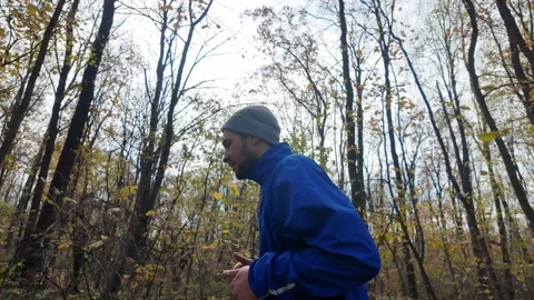 Side view of man jogging in autumn forest, wearing blue jacket and beanie Stock Footage 318174800