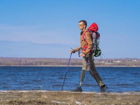 Side view of a man with prosthesis of a leg walking by the river. Nordic walk Stock Photos