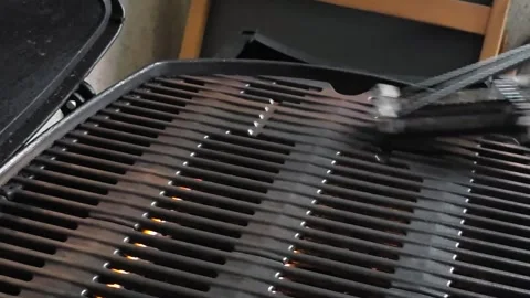 Side view of a man scrubbing a lit barbecue grill with a wire brush, flames.. Video stock 342747689