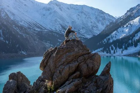 Side view of a man sitting on a boulder on a vantage point over mountain lake Stock Photos